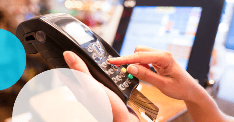 A hand holding a card-payment terminal at a shop counter
